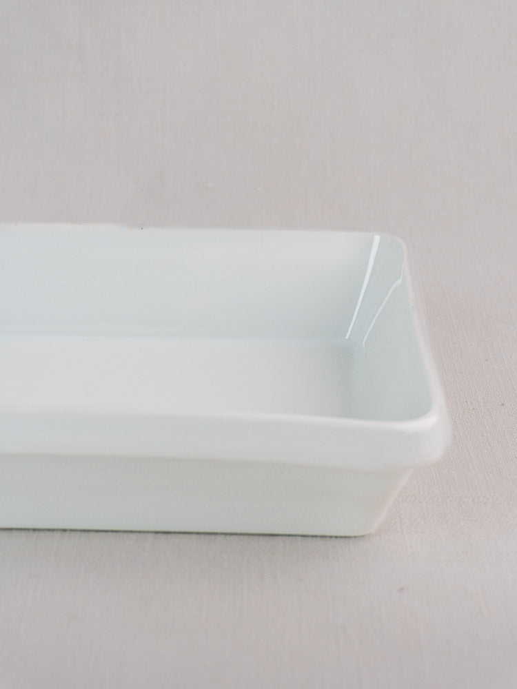 Partial view of vintage French white porcelain baking dish, rectangular shape on a light beige background.