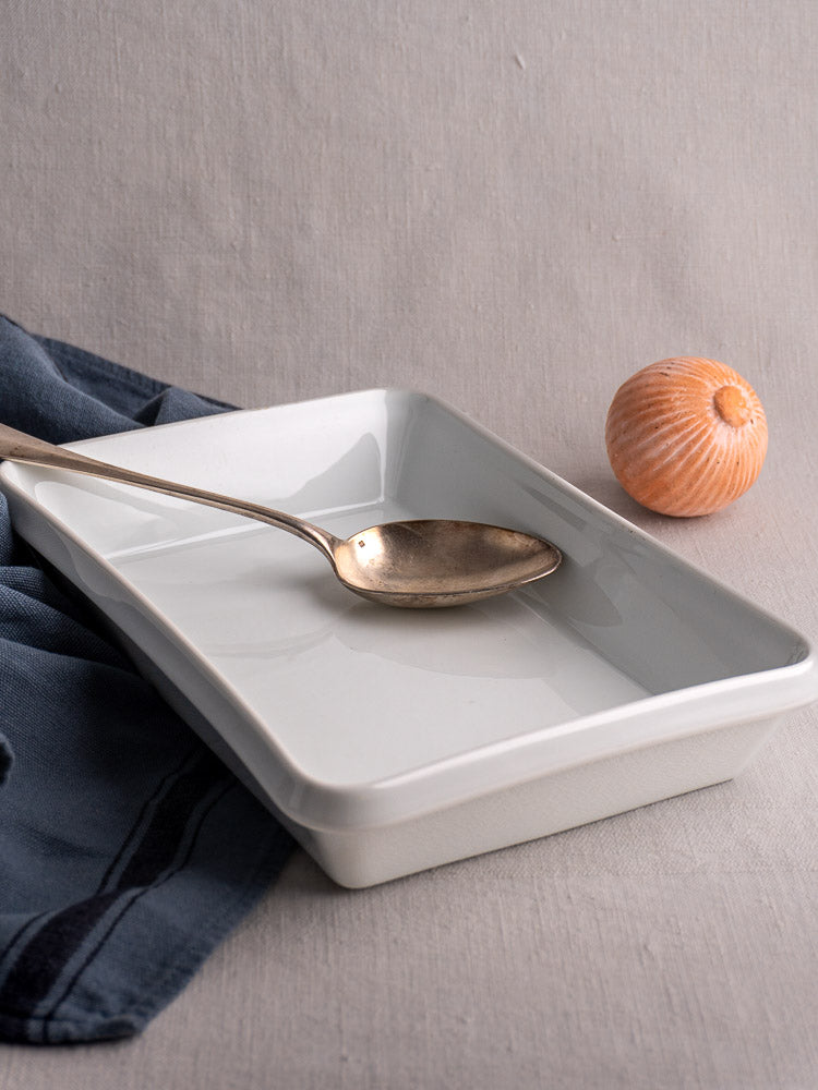 Vintage French white porcelain rectangular baking dish on a light, textured surface with neutral background.