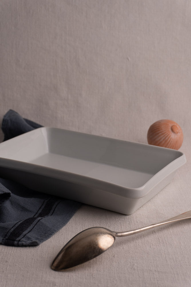 Vintage French porcelain white rectangular baking dish on textured off-white surface with napkin and spoon.