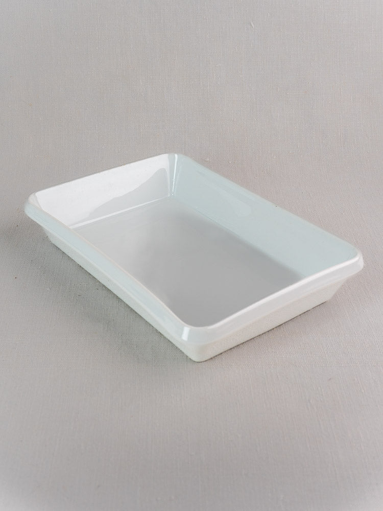 Vintage French porcelain baking dish, rectangular and white, on a light grey textured background.