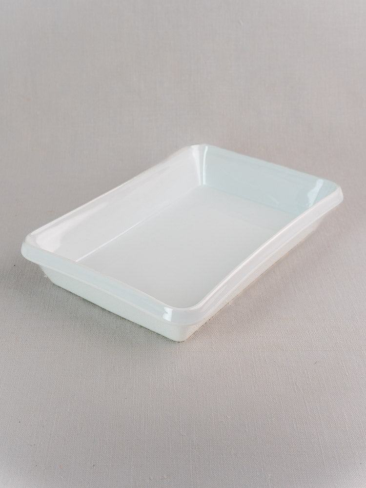 White vintage French porcelain baking dish, rectangular and empty, on a light-grey textured background.