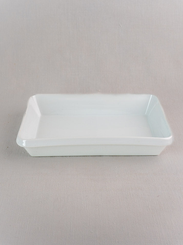 Vintage French porcelain baking dish with angled sides, glossy white finish, on light gray fabric.