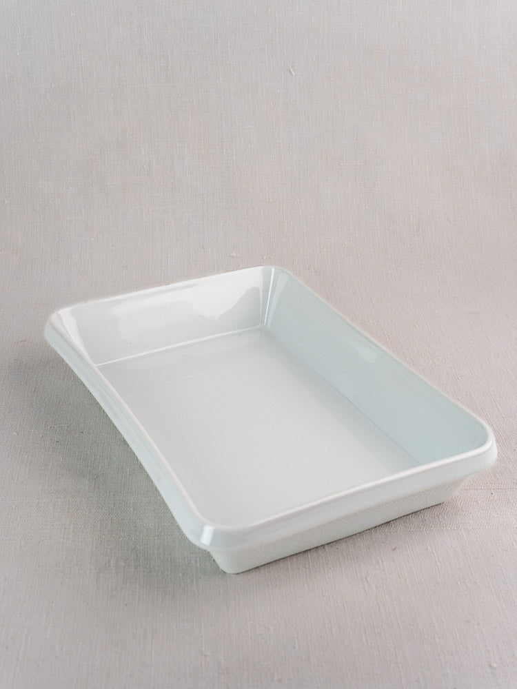 White French porcelain baking dish with slightly curved sides on a light gray textured surface.