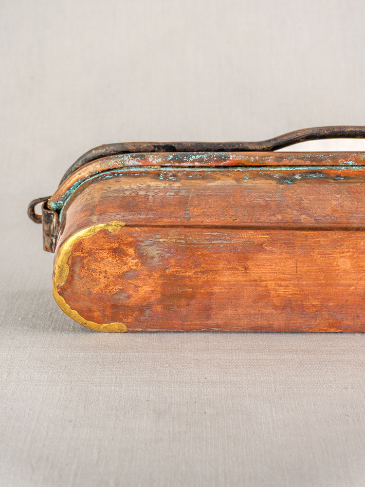 Antique French copper poissonniere with rounded end, patina, and brass-colored repairs on neutral fabric background.