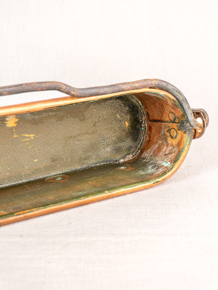 Antique French copper poissonniere fish kettle with metal handle and aged patina, resting on light fabric.