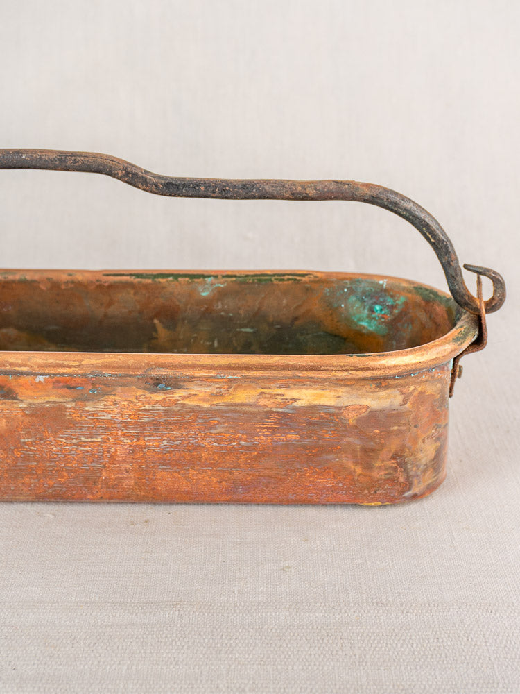 Antique French copper poissonniere fish kettle, 19th century, with weathered patina and curved handle on neutral fabric background.