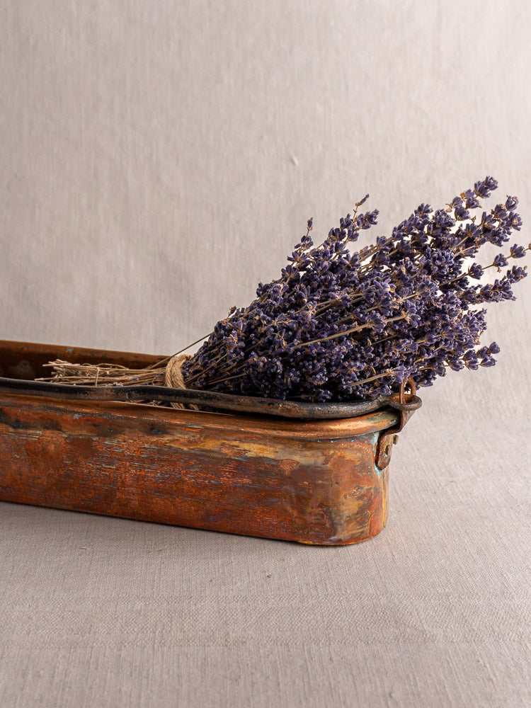 Antique French copper poissonniere with bundled dried lavender, displayed on a light gray fabric surface.
