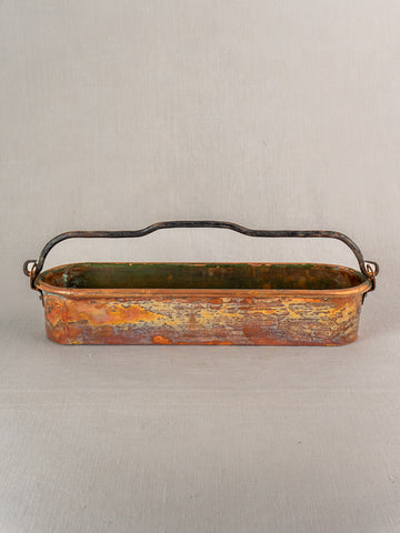 Antique French copper poissonniere with weathered patina and dark curved handle on a light gray background.