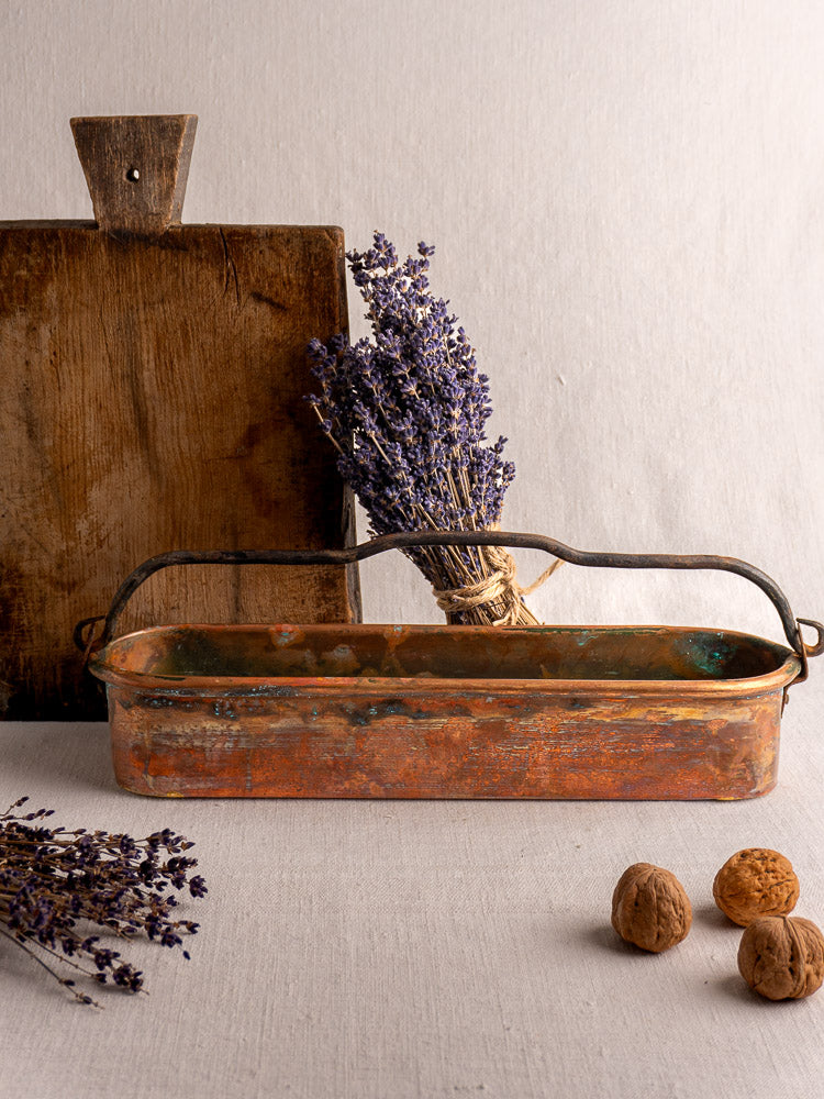 19th-century French copper poissonniere with handle, shown before a wooden board, dried lavender, and walnuts.