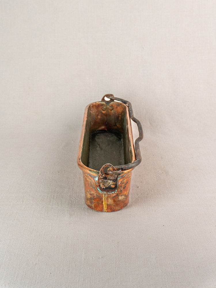 19th-century French antique copper poissonniere fish kettle with weathered patina and curved handle on neutral fabric background.