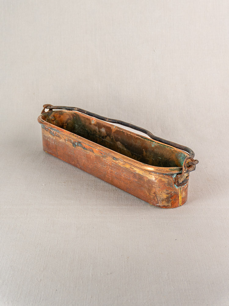 19th-century French copper poissonnière fish kettle with dark handle and patina on neutral fabric background.