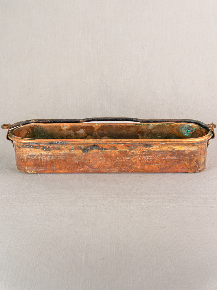 Antique French copper poissonniere fish kettle with two small handles and aged patina on a light surface.