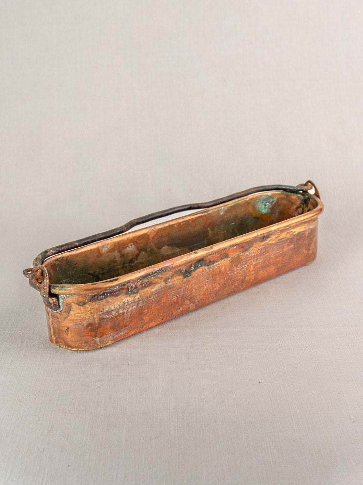 Antique French copper poissonnière fish kettle, long and rectangular with tarnished finish and end handles on neutral fabric.