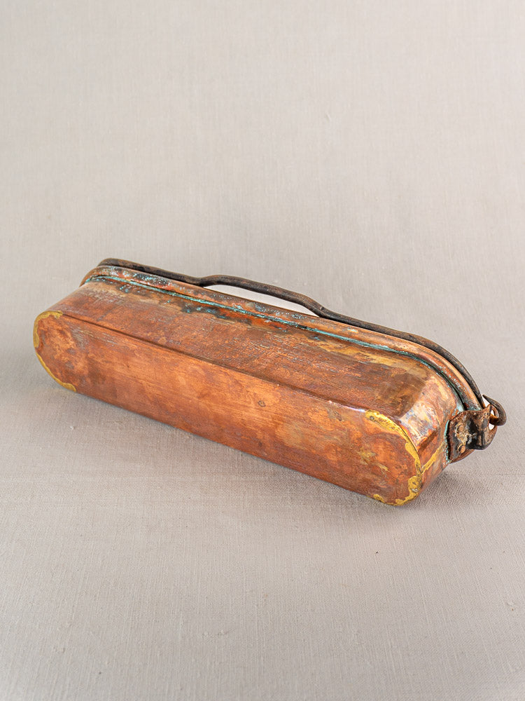 Antique French copper fish kettle with curved handle and worn corners on a light grey fabric surface.