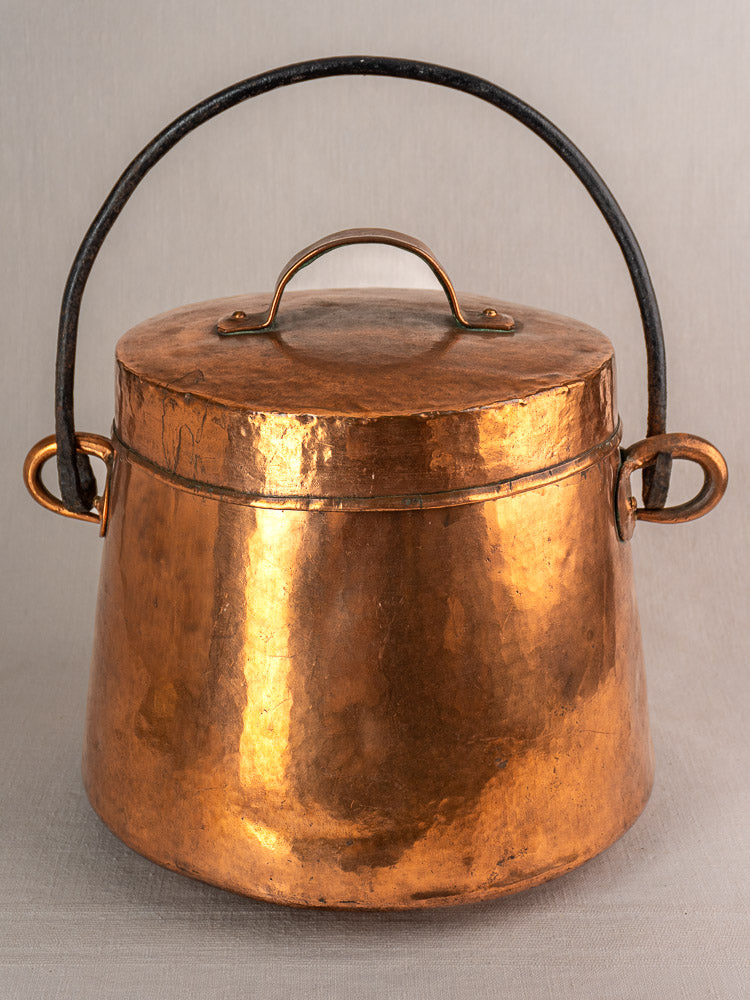 Antique French hand-hammered copper cauldron with lid, thick black handle, and side handles on a neutral background.