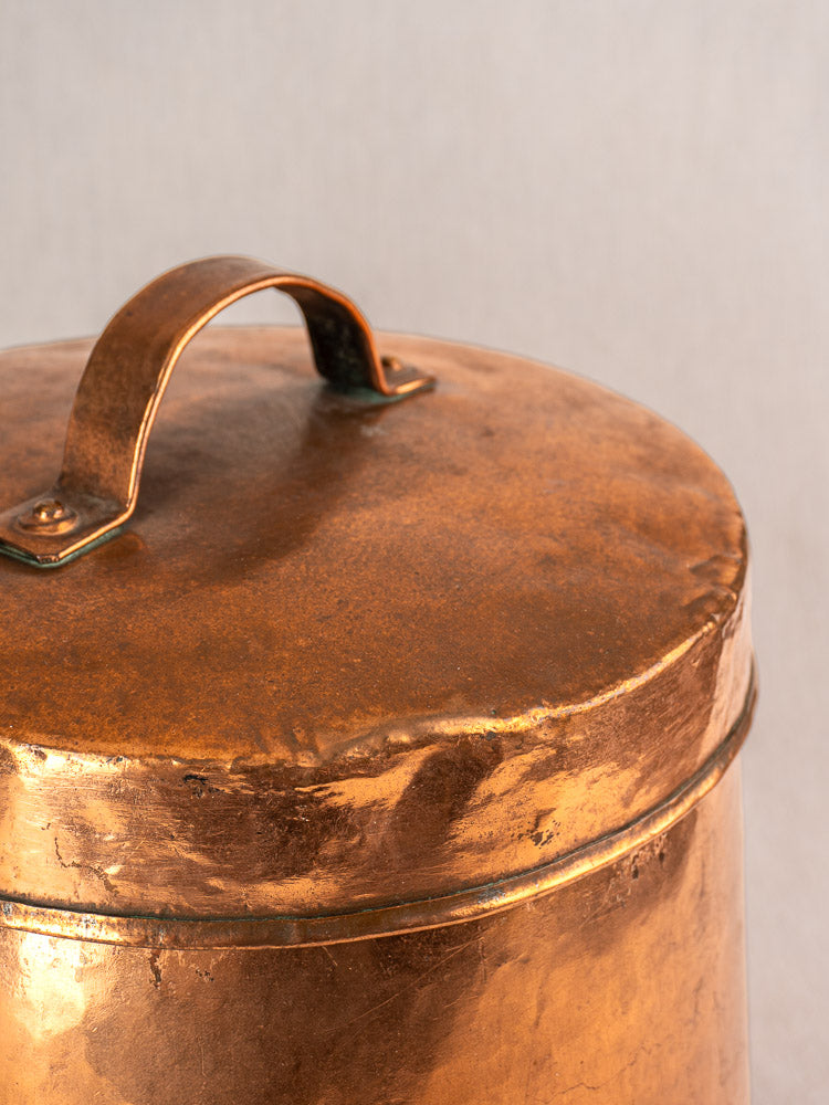 Antique French copper cauldron, 19th-century hand hammered marmite with lid and curved handle, on beige background.