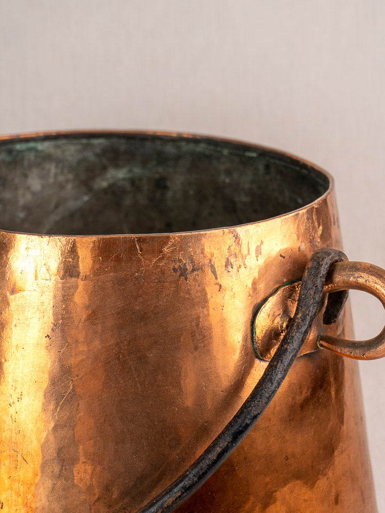 Antique French copper cauldron with lid, hand hammered, dark handle, rich patina and tarnish on neutral background.