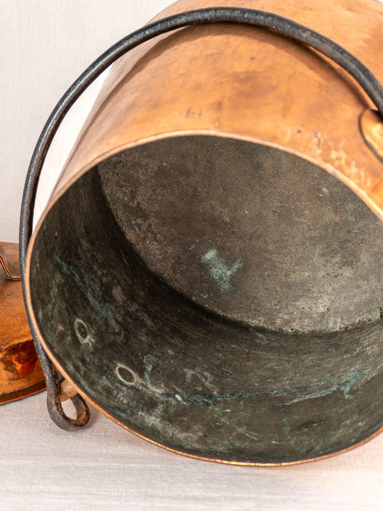 Antique French copper cauldron with hand-hammered lid, dark patina, and curved handle showing age and oxidation.