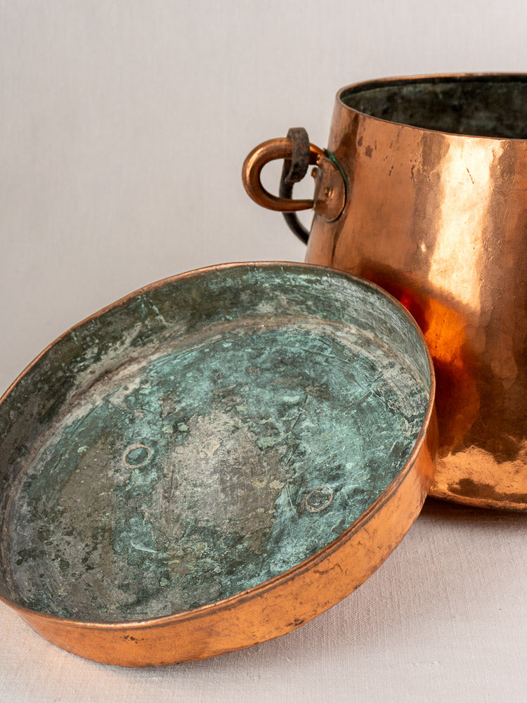 Antique French copper cauldron, hand-hammered 19th-century lidded marmite with green-patina lid on light surface.