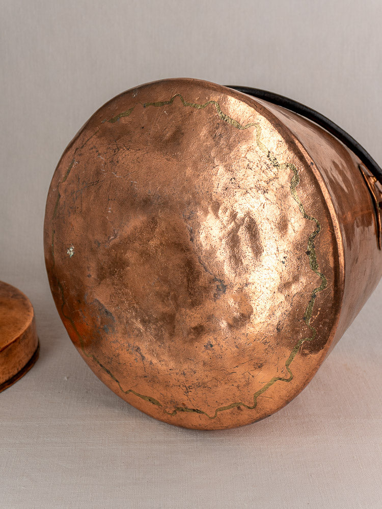 Antique French copper cauldron base with tarnished, hammered surface and green oxidation on edges, on light fabric.