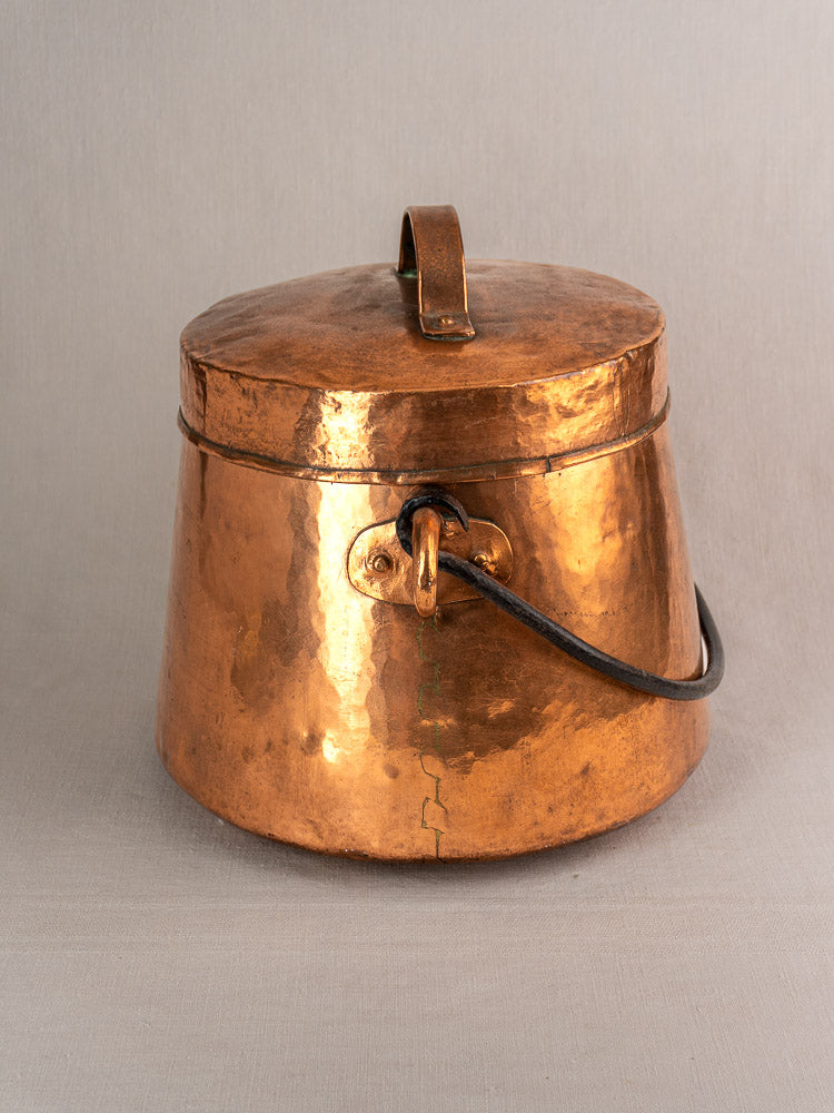 19th-century antique French copper cauldron with hand-hammered lid, curved handles, and flared base on gray surface.