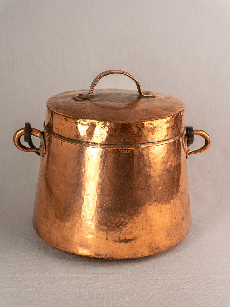 Large antique French hammered copper cauldron with lid and side handles, classic 19th-century design, on a neutral background.