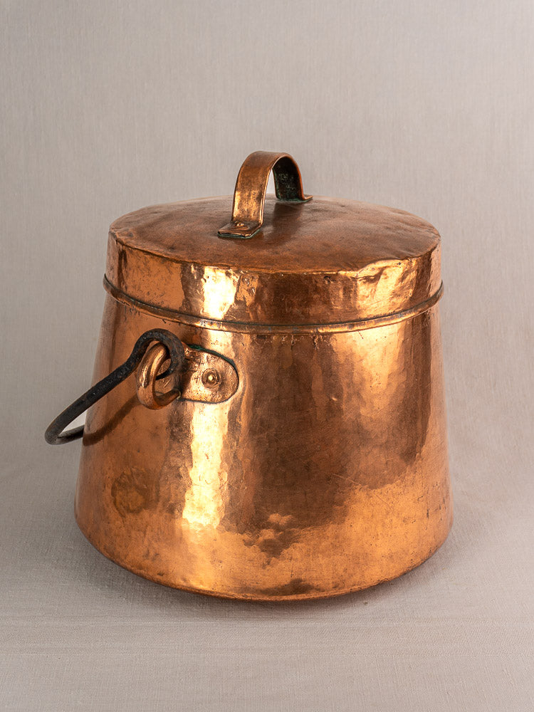 Antique French hammered copper cauldron with side handle and fitted lid, displayed on a light background.