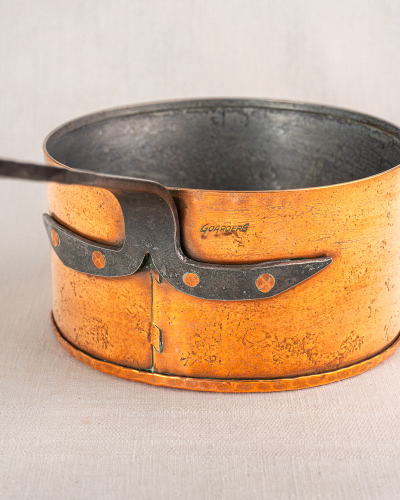 Set of four vintage French Jean Goardère copper saucepans with decorative side latches on light fabric.