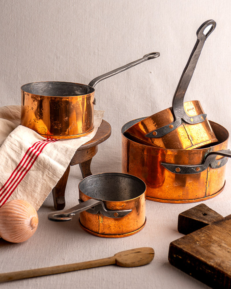 Set of four vintage Jean Goardère French copper saucepans with metal handles on light surface.