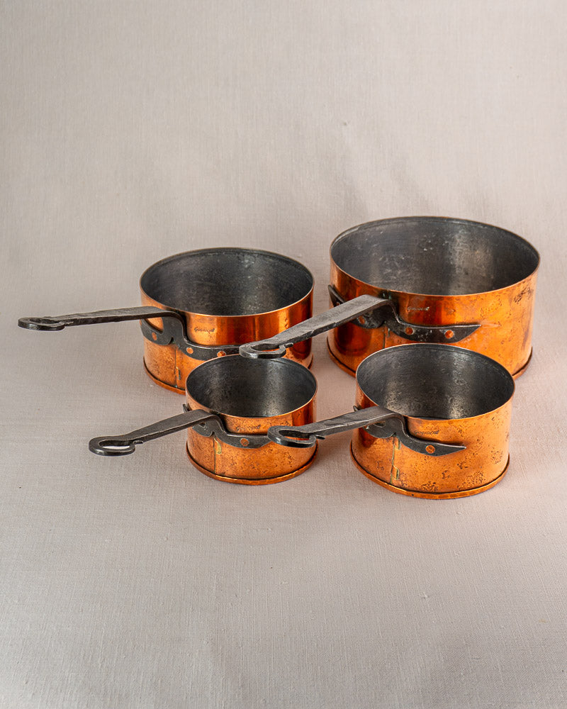 Set of four vintage Jean Goardère French copper saucepans with black metal handles, nested on light surface.