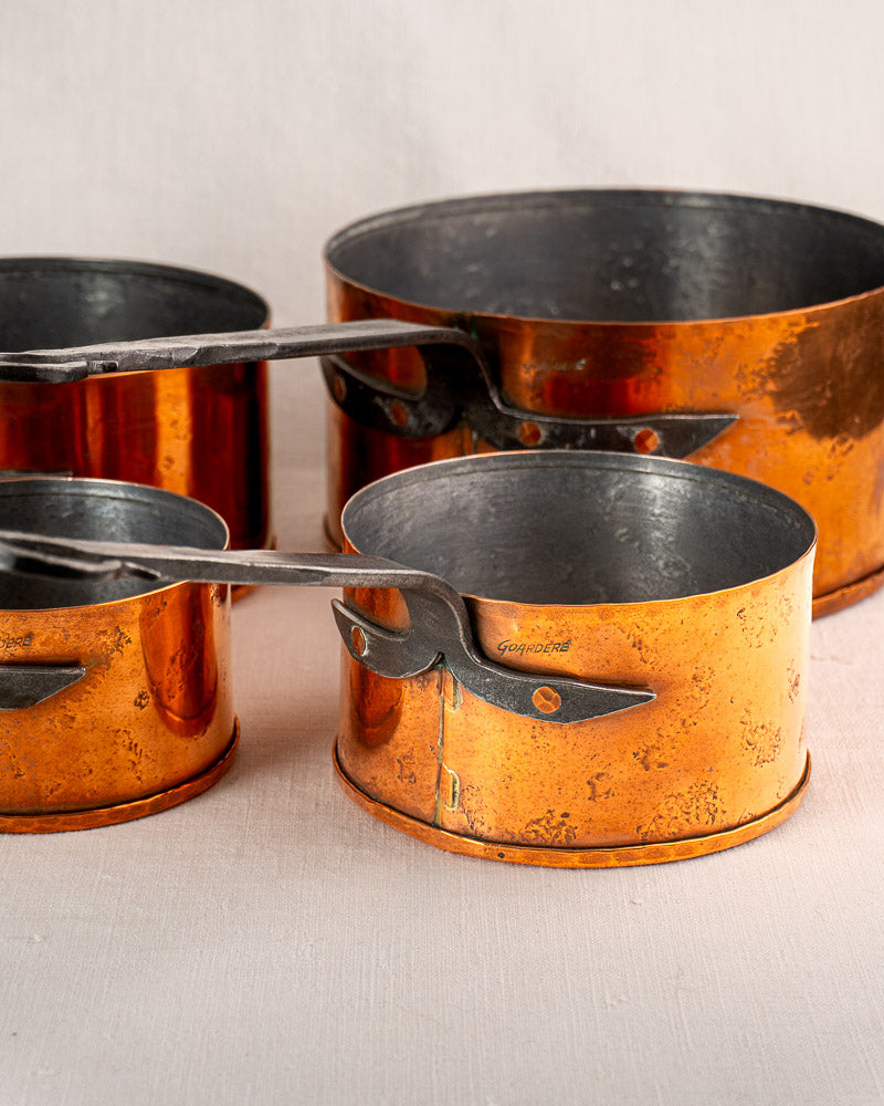 Set of four vintage Jean Goardère French copper saucepans with black handles, lightly tarnished.