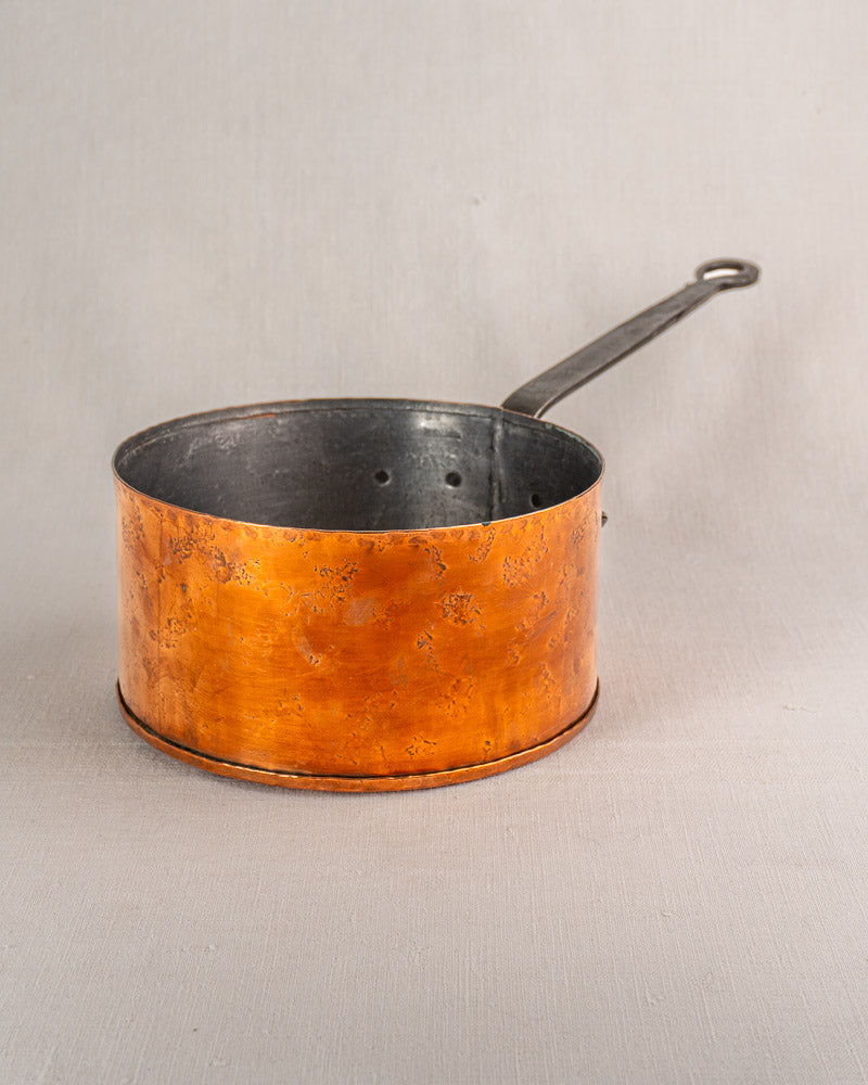Jean Goardère vintage French copper saucepan with black metal handle and worn, tarnished finish on light grey surface.