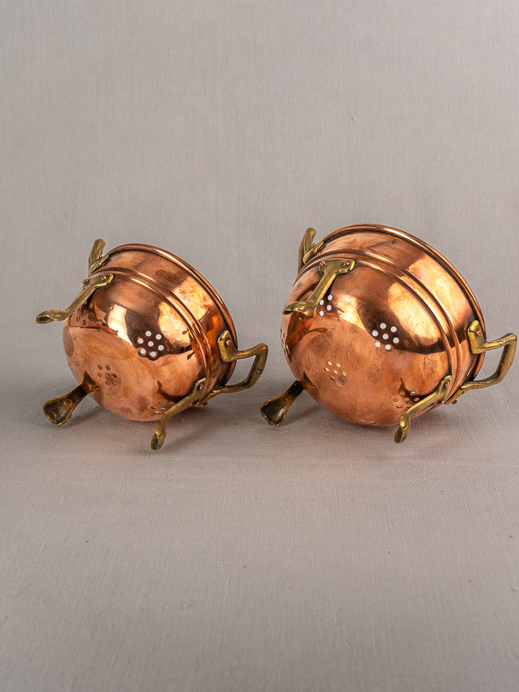 Set of three antique French copper colanders with brass paw feet, small holes, and slightly tarnished finish.