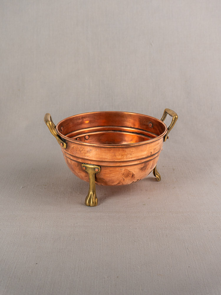 Antique French copper colander with brass paw feet and handles, early 20th century, on a light gray surface.