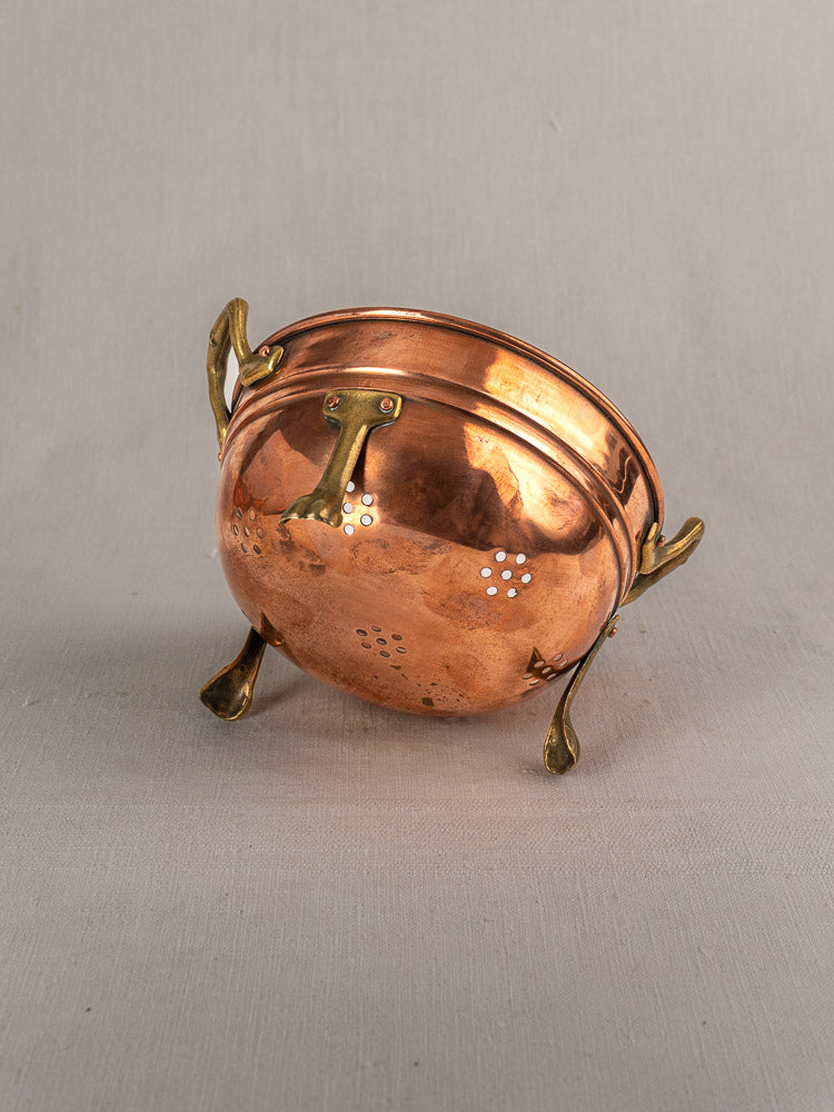 Set of three antique French copper colanders with brass paw feet, curved handles, and decorative vent holes on a gray background.
