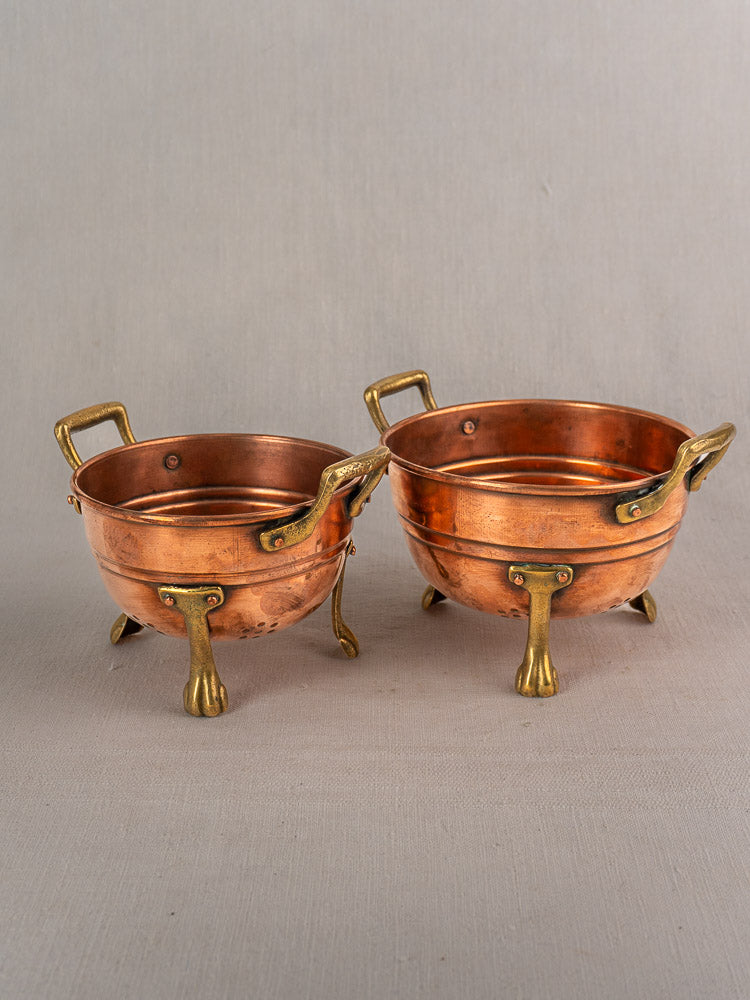 Set of three antique French copper colanders with brass paw feet, early 20th century, on neutral fabric.