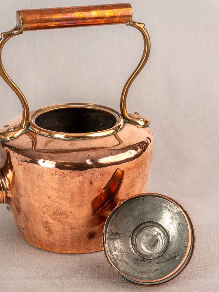 Antique French copper tea kettle with wood handle, acorn finial lid beside, showing rich patina and gentle wear.