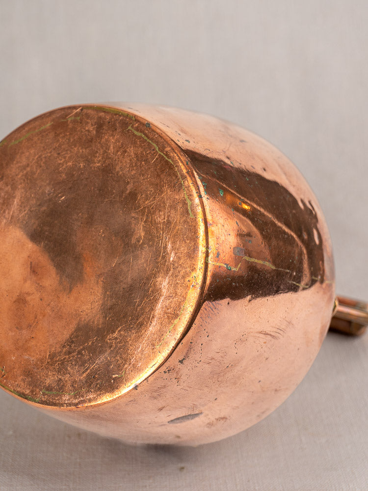 Antique French copper tea kettle with worn, tarnished bottom and partial wood handle visible on the right.