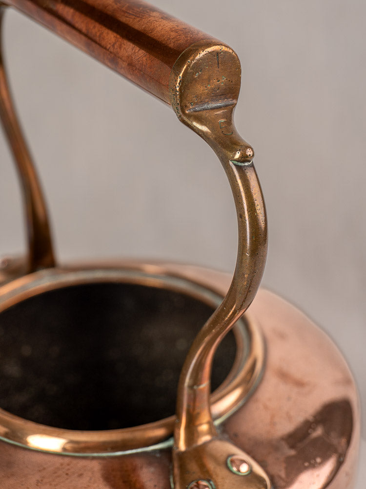 Antique French copper tea kettle with wood handle and brass acorn finial, patina visible, on soft gray background.