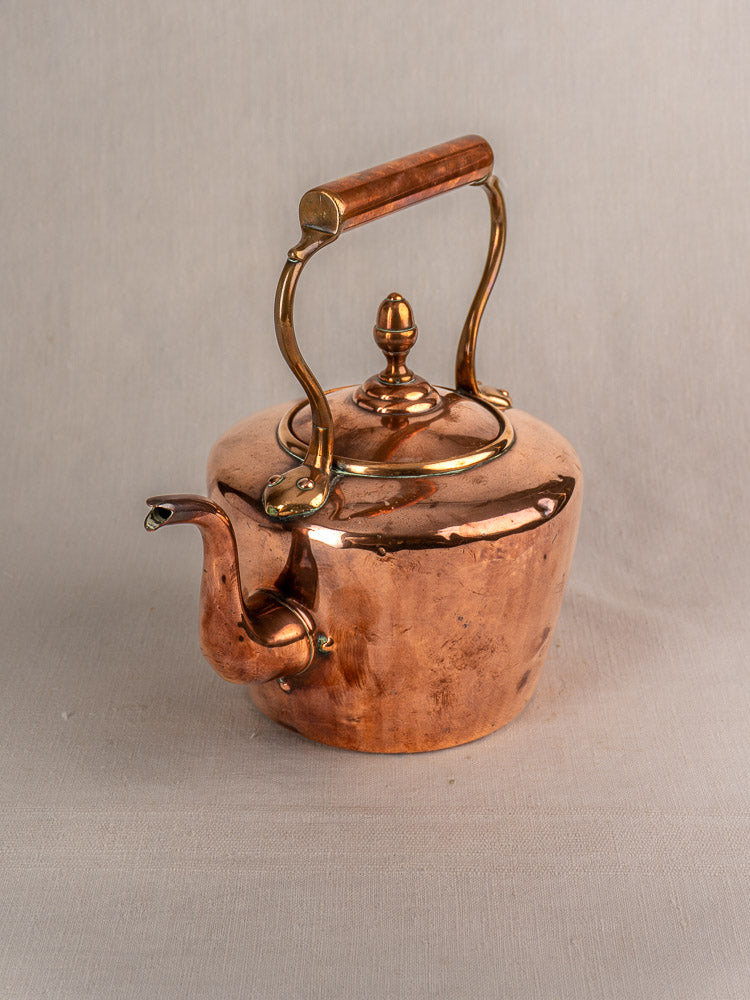 Antique French copper tea kettle with rounded body, wood handle, gooseneck spout, brass acorn finial on light background.