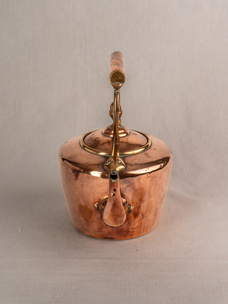 Antique French copper tea kettle with wood handle, late 19th century, on a light gray fabric surface.