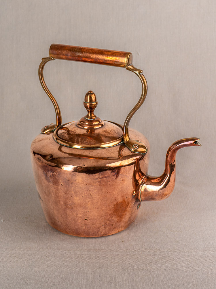 Antique French copper tea kettle with gooseneck spout and wood grip handle on neutral fabric background.