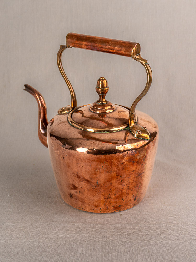 Antique French copper tea kettle with wood handle, late 19th century, shows wear and tarnish on neutral gray background.