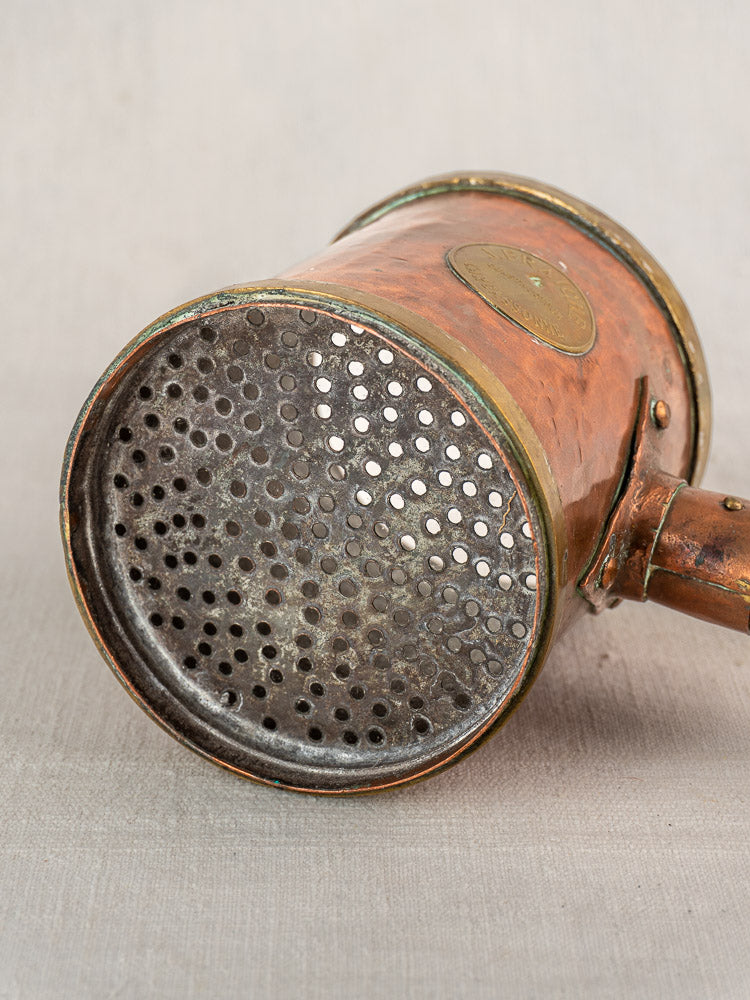 Antique French copper strainer pot by L. Fraiche Carcassonne with perforated lid and short handle on light textured surface.