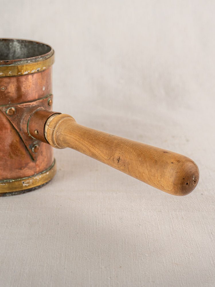 Antique French copper strainer pot with wooden handle, partial perforated wall, resting on light fabric.