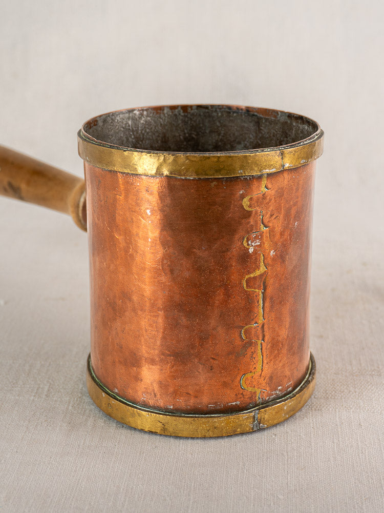 Antique French copper strainer pot by L. Fraiche Carcassonne with brass bands and wood handle on neutral fabric.