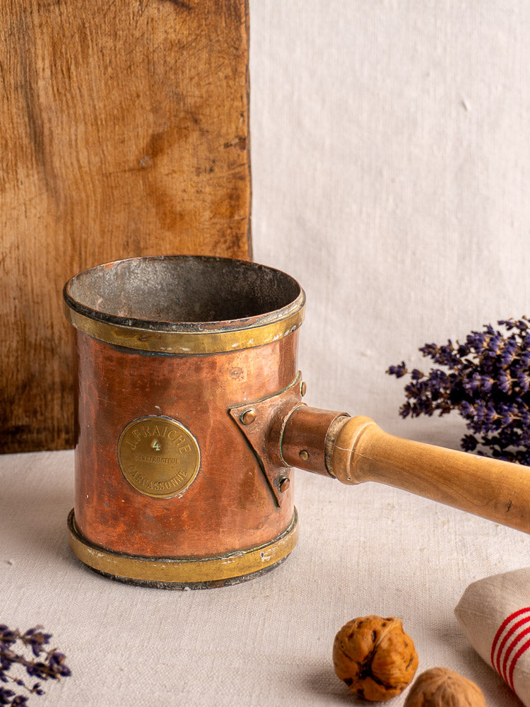 Antique French copper strainer pot by L. Fraiche Carcassonne, cylindrical with wooden handle, on neutral fabric background.