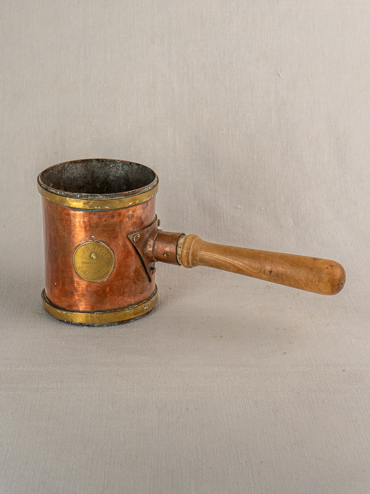 Antique French copper strainer pot by L. Fraiche Carcassonne, cylindrical with wooden handle, on neutral fabric background.