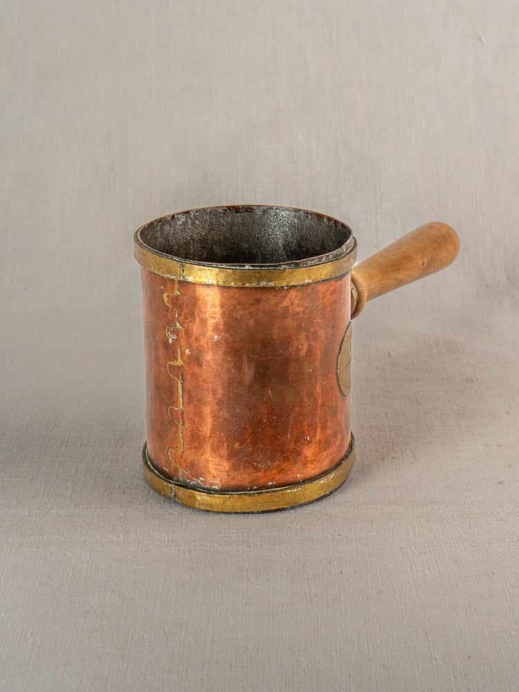 Antique French copper strainer pot with cylindrical body, wooden handle, and visible seams on neutral textured surface.