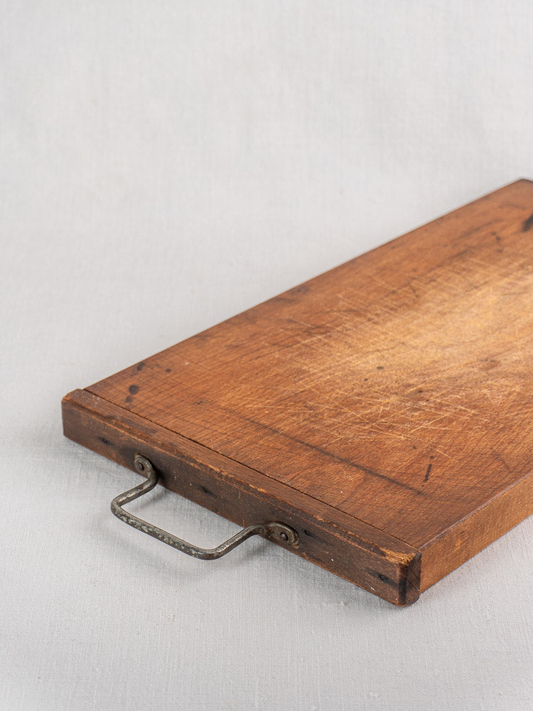 Antique French wooden cutting board with iron handle and vintage knife marks, displayed on a light gray surface.